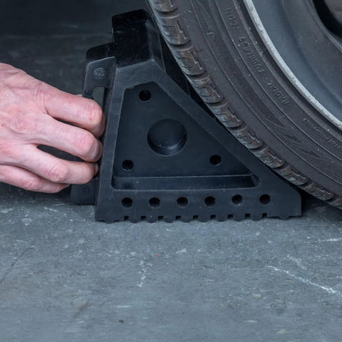 Solid Rubber Wheel Chocks With Traction Ribs For That Tire Grip And A Handy Handle For Quick Positioning Built Tough To Keep Your Ride Secured On Slopes placed behind a vehicle tire on concrete surface