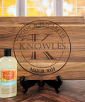 Personalized wooden cutting board with circular KNOWLES engraving, date May 21, 2024, on a stand; oil included