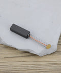 Close-up of a single carbon brush, spring-loaded design, for TE 17 model power tool motor 24x8x6.4mm, resting on a stone surface.