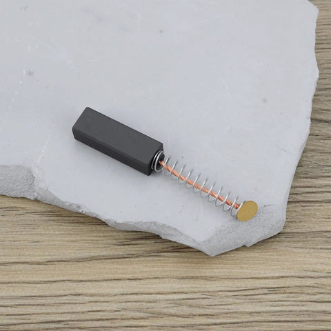 Close-up of a single carbon brush, spring-loaded design, for TE 17 model power tool motor 24x8x6.4mm, resting on a stone surface.