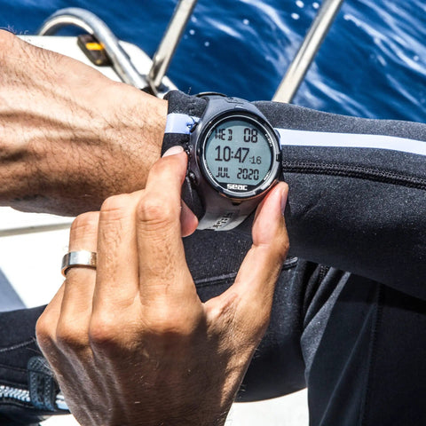 Person adjusting wrist-worn scuba and freediving dive computer with logbook display, Get Your Hands On This Awesome Scuba And Freediving Dive Computer That Comes Packed With A Handy Dive Logbook Smart Dive Planner Essential Safety Alarms And Heart Rate Monitoring To Keep You Safe And Stylish On Every Dive.