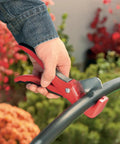 Drip Tubing Cutter And Punch Gun Kit For 1 Inch Flexible Tubing cutting irrigation pipe in garden setting with red-handled tool.