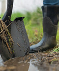 Short-Handle Digging Shovel With Heavy Duty Carbon Steel Build in use, showing serrated edge in muddy ground, rubber boot visible