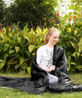 Person sitting outside wrapped in XL Widened Upgraded 4 Season Camping Sleeping Bag For Adults And Kids Built Tough Waterproof Lightweight 0F Warmth