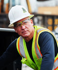Sick Clear Vision Transition Safety Glasses With Anti Fog Coating And Scratch Resistant Lenses Featuring Adjustable Non Slip Fit For Legit All Day Comfy ANSI Certified Protection worn by a male worker in a hard hat and high-visibility vest.