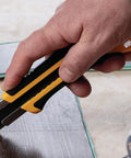 Extra Heavy-Duty 25mm Utility Knife With Ratchet Lock, Razor-Sharp Blade And Seven-Stage Snap-Off System, Fiberglass-Reinforced Handle, Built-To-Last Workhorse For Industrial Construction And Shop Projects. cutting a board