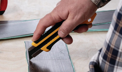 Extra Heavy-Duty 25mm Utility Knife With Ratchet Lock, Razor-Sharp Blade And Seven-Stage Snap-Off System, Fiberglass-Reinforced Handle, Built-To-Last Workhorse For Industrial Construction And Shop Projects. cutting a board