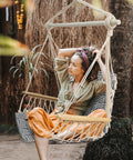 Woman sitting in upgraded hammock chair with wooden armrests and steel spreader bar, cotton woven fabric, outdoor setting