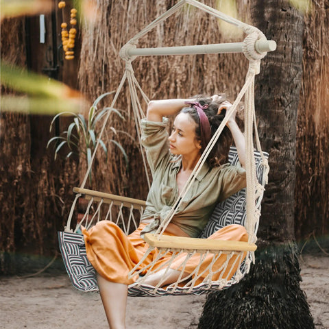 Woman sitting in upgraded hammock chair with wooden armrests and steel spreader bar, cotton woven fabric, outdoor setting
