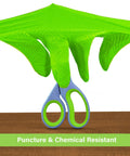 Neon green disposable glove with raised diamond grip gripping blue-handled scissors