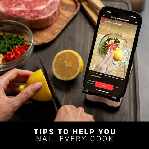 Person slicing lemon next to smartphone displaying recipe instructions, illustrating use of 100 Percent Wireless Smart Meat Thermometer With Dual Temp Sensors And Guided Cook System For Barbecue Grill Oven And Smoker No Wires No Fuss 165 Ft Bluetooth Range Dishwasher Safe app.