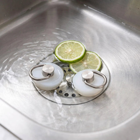 White Silicone Drain Stopper for Bathtubs and Holes in stainless steel sink with sliced lime.