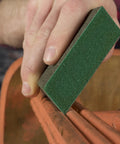 Hand using Medium 80 Grit Dual Angle Sanding Sponge 3x5x1 Inch for wet or dry use on wooden surface, flexible handheld pad with grit on all sides.