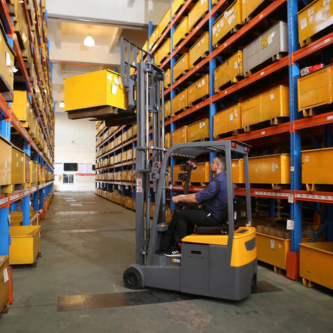 Super Reliable Electric Seated Forklift With 3300 Pound Capacity lifting a yellow box in a warehouse aisle.