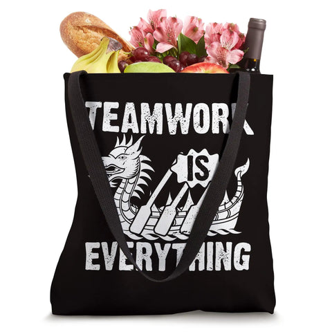 Black tote bag with 'Teamwork Is Everything' text and dragon graphic, filled with groceries. Teamwork Is Everything Tote Bag For Paddling Crew Fans Race Day Gear And Training Sessions Big Enough For Gear And Water Vibe Print Tough Canvas Tote For Adrenaline Fueled Practices And Weekend Meetups.