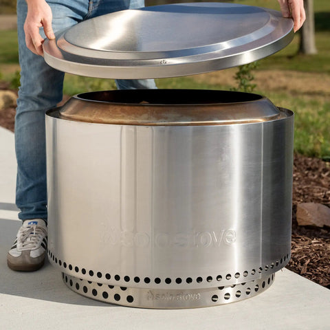 Person placing Yukon Lid Fire Pit Cover Premium 304 Stainless Steel Round Tabletop Accessory on a fire pit