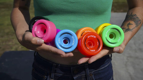 Person holding multi-colored Zen Quad Roller Skate Wheels 4 Pack 32mm x 62mm 85A Durable Urethane Black For Rink Street And Sidewalk Use