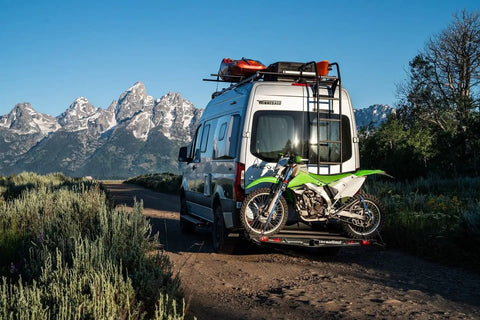 Dirt Bike Hitch Carrier With Ramp For 2 Inch Class III And IV Hitches, Up To 500 Lb Capacity, Includes Ramp And Four Tie Down Eyelets For Secure Motorcycle Transport on a van in a mountainous area.