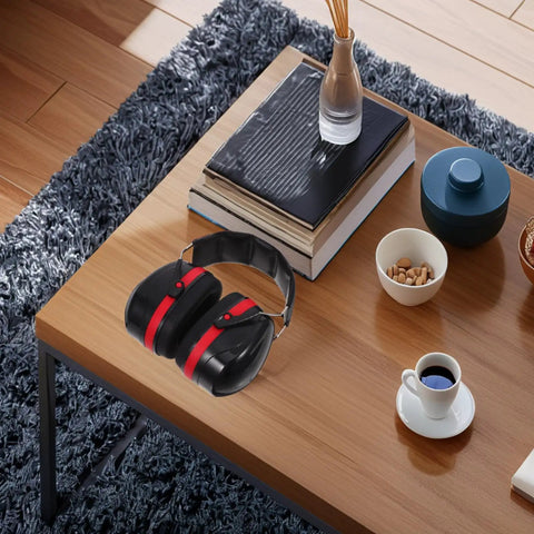 Black and red double layer over ear earmuffs on a wooden table, designed for construction mowing and shop jobs.
