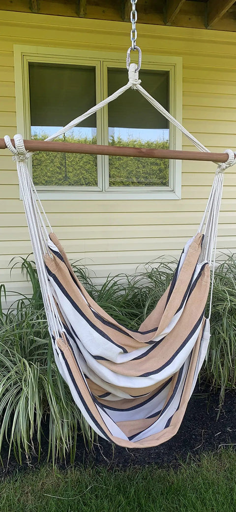 Striped hammock chair hanging outdoors with greenery and wall background.
