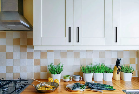 Kitchen setting with 30 Pack Solid 5 Inch Square Cabinet Handles Matte Black Pulls for kitchen cabinets, shown installed on white cabinets above countertop with plants.