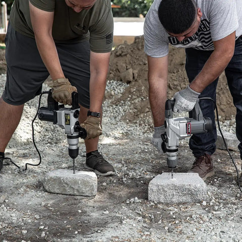 Two men using Electric SDS-Plus Rotary Demolition Hammer 1180W With 1-1/4 Inch Bit Capacity on concrete blocks outdoors
