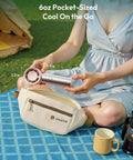 Person holding Compact Handheld Personal Fan With Turbo Wind On The Go USB Rechargeable Mini Cooler outdoors next to a pouch.