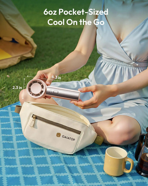 Person holding Compact Handheld Personal Fan With Turbo Wind On The Go USB Rechargeable Mini Cooler outdoors next to a pouch.