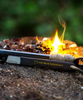 Prepper-Ready Large 6 Inch Ferro Rod With Tungsten Carbide Striker And Sharpener next to campfire on bark.