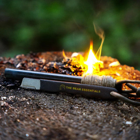 Prepper-Ready Large 6 Inch Ferro Rod With Tungsten Carbide Striker And Sharpener next to campfire on bark.