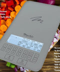 Digital kitchen scale on counter with vegetables, features built-in nutrition calculator, backlit LCD, 11 lb capacity for meal prep.