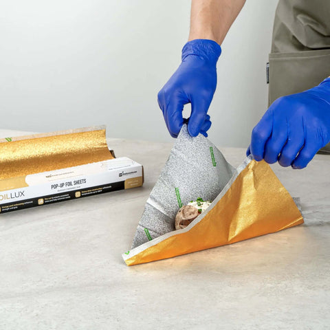 Person using Gold Embossed Pop-Up Foil Sheets 10.8 X 9 Inch interfolded greaseproof foil for wrapping food on counter.