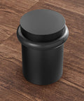 Heavy Duty Solid Steel Floor Door Stopper Matte Black Wall Protector Rubber Bumper on wooden floor, cylindrical design, top view.