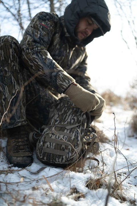 Pro 1075 Backpack in Mossy Oak Bottomland Camo with hunter in snow, showing wide padded shoulders, and rugged outdoor design