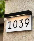 Solar Powered LED Address Sign For Outdoor Use With 3000K Warm White Light, Wireless Waterproof House Numbers Plaque That Illuminates At Night, Auto On Feature, 2000mAh Battery Delivers 40 Hours Of Brightness, No Wires Needed on brick wall