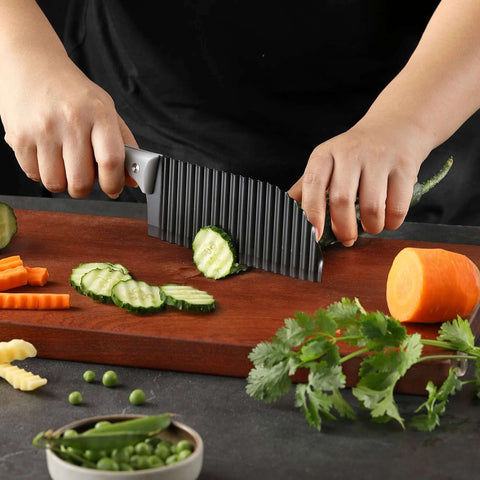 Front view of crinkle-cut knife with ribbed dark blade and gray rubber handle slicing cucumber on a wooden board