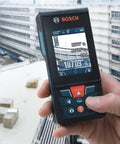 Hand holding Beast Of A Blaze Outdoor Connected Laser Measure With 400 Ft Range, 5 MP Digital Viewfinder at construction site