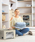 Person holding folded clothes with beige stackable storage bins with metal frame for closet organization in the background.