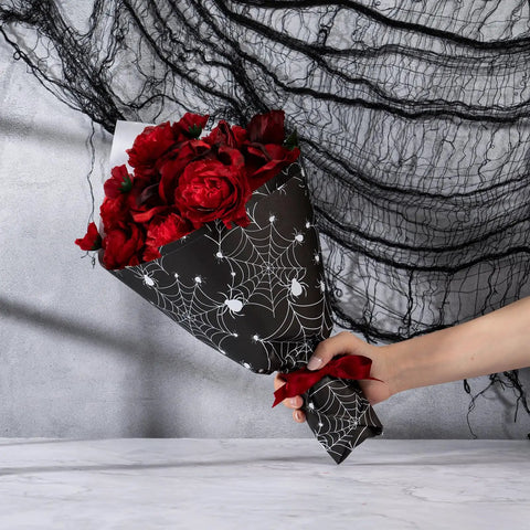 Spooky Spider Web Floral Wrapping Paper 18x18 Inches Black White Bouquet Wrap for Halloween Gifts held with red roses.