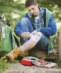 Front view: outdoors, person tending knee with General Medi 2-in-1 First Aid Kit (215 pc) and mini kit, red case open.