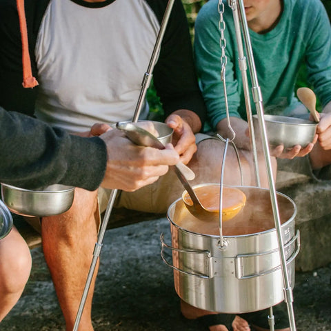 Campfire 2 Pot Wood Burning Camping Stove Set For 4 Plus People in use, with people serving stew outdoors, no batteries needed.