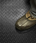 Foot in boot on Black Embossed Diamond Plate Pattern Floor Runner Protector, 27 Inches Wide By 25 Feet Long, Heavy Duty Plastic Shield For Hardwood And Laminate Floors, Resists Dings And Spills, Easy To Cut, Made In The USA.