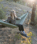 Person relaxing in a green camping hammock with 400 lb capacity and heavy duty straps among trees, highlighting a peaceful setting.