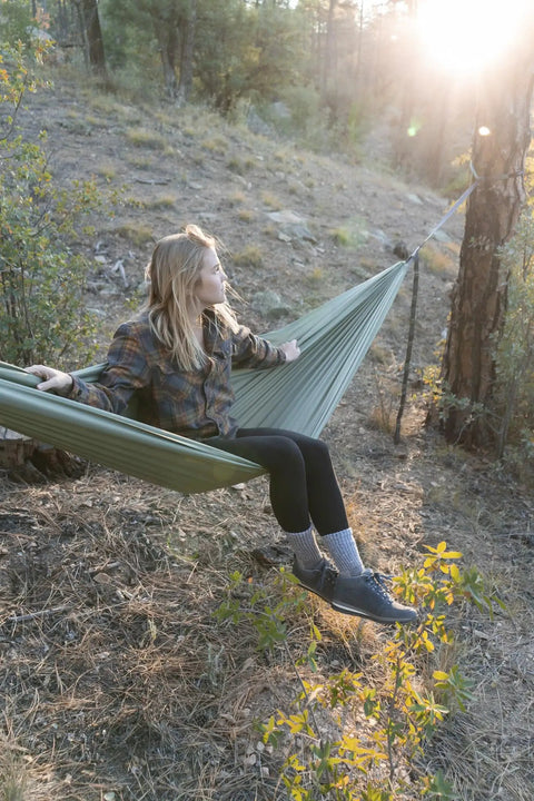 Person relaxing in a green camping hammock with 400 lb capacity and heavy duty straps among trees, highlighting a peaceful setting.
