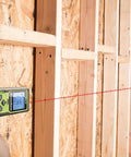 Pro Grade Laser Distance Meter 325 Ft in use measuring distance on wooden studs with backlit display.