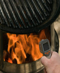 Using a No Touch Infrared Thermometer For Cooking And BBQ Laser Temperature Gun With Digital Display next to a fire pit.