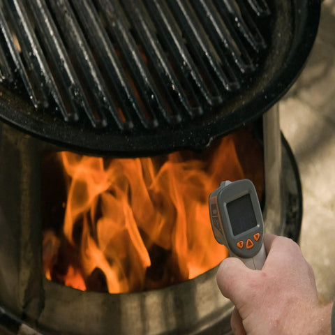 Using a No Touch Infrared Thermometer For Cooking And BBQ Laser Temperature Gun With Digital Display next to a fire pit.