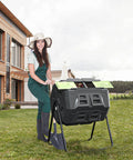 Woman using Two Chamber Outdoor Compost Tumbler Bin With Built In Thermometer For Easy Temperature Monitoring, Rotates Smoothly On Sturdy Steel Frame, 43 Gallon Capacity Split Into 2 X 21.5 Gal Compartments, Green Door in garden