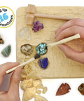 Hands using tools to uncover gems from Gem Stone Dig Kit With 16 Real Gems And Crystals Including Quartz Point And Amethyst STEM Education