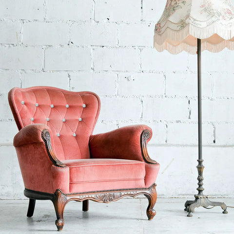 Vintage pink armchair with crystal upholstery nails tacks set on tufted backrest beside a floral lamp, elegant decor.